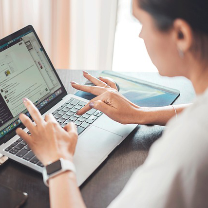 Frau sitzt am Tisch vor geöffnetem Laptop